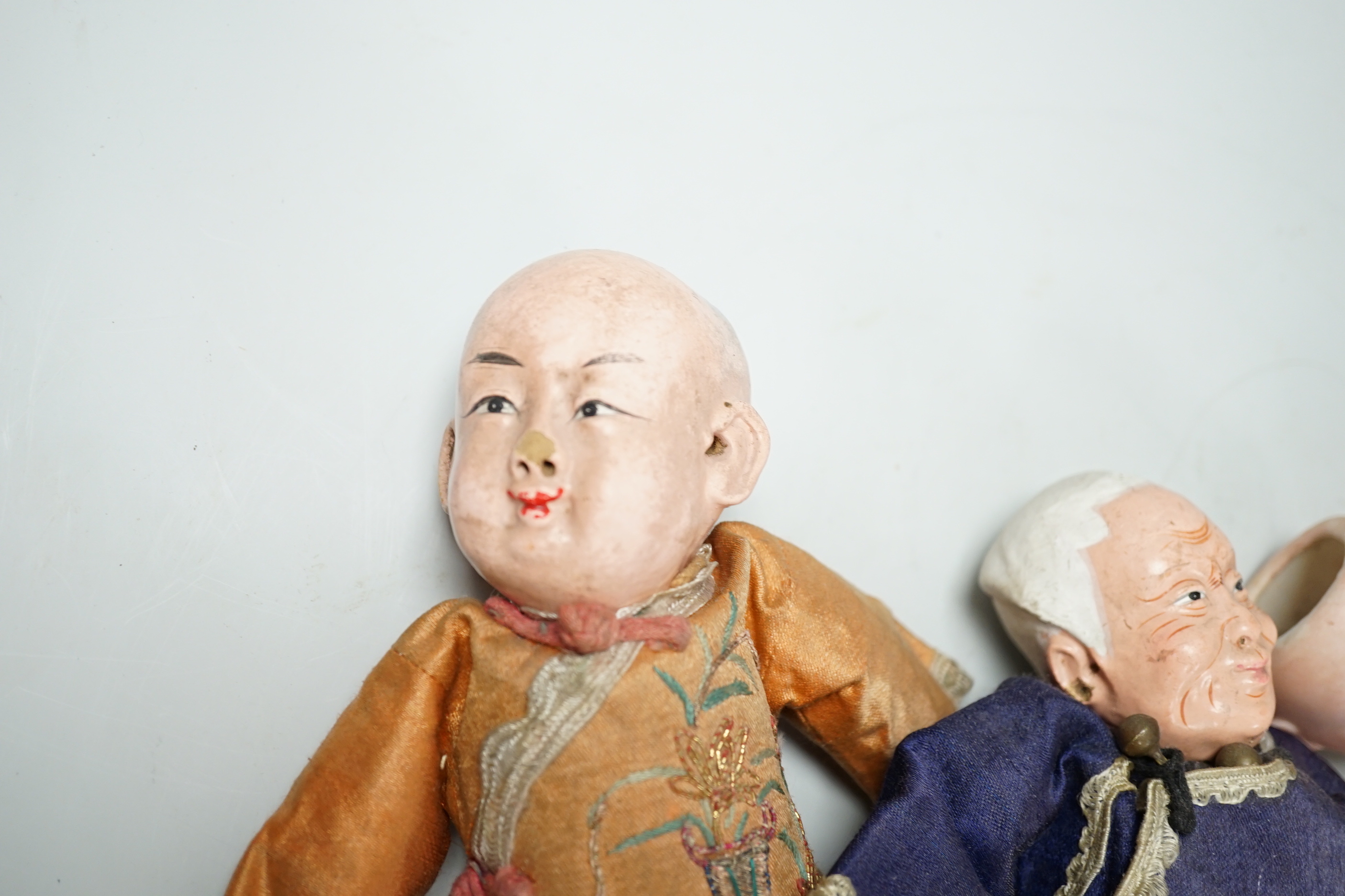 Two Chinese Papier mache dolls with embroidered silk clothing, a pair of Chinese embroidered silk slippers, a similar child’s bonnet a pair of Japanese slippers and three other dolls